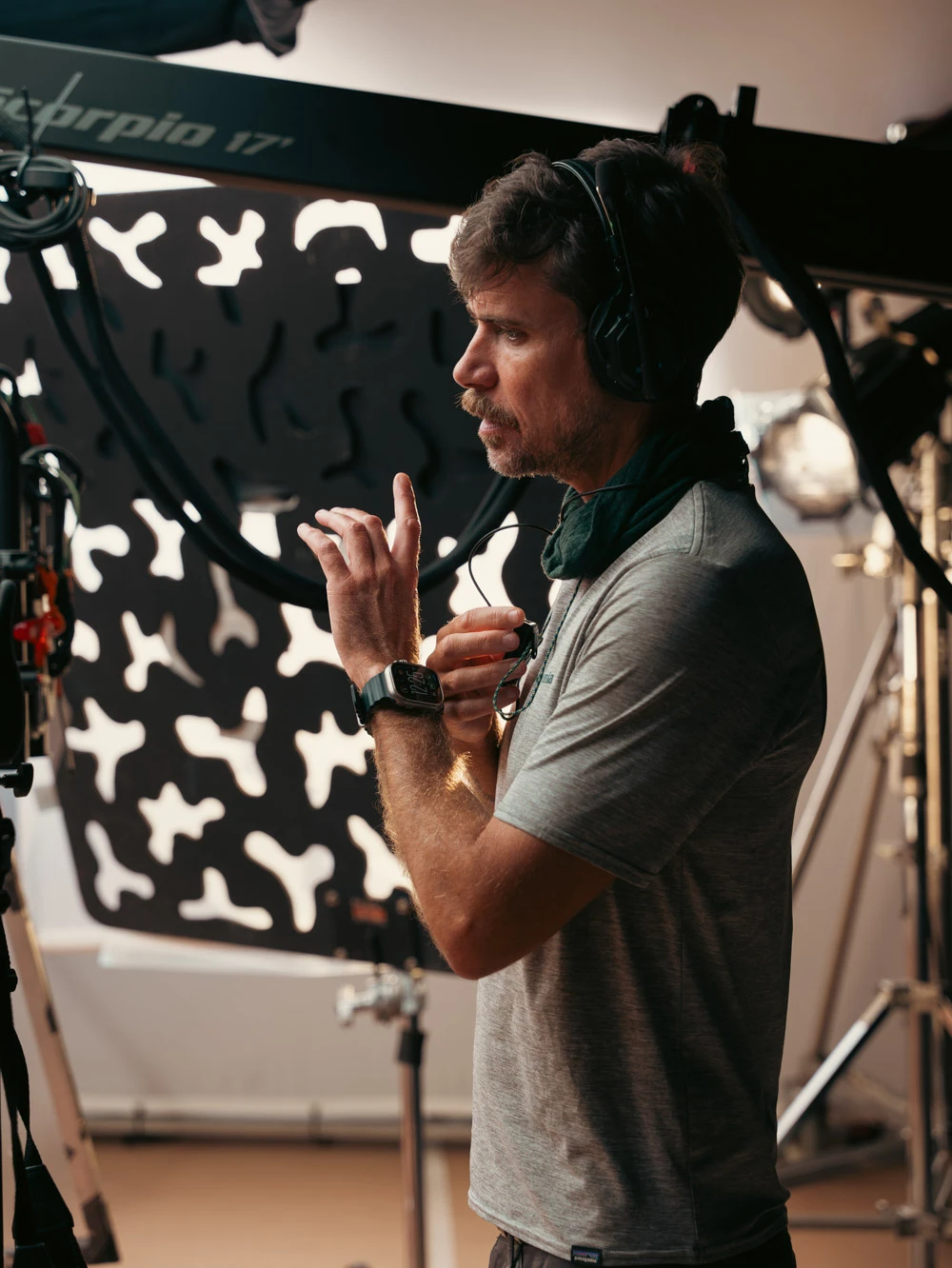 Crew member with a headset giving directions beside a camera crane and a lighting gobo